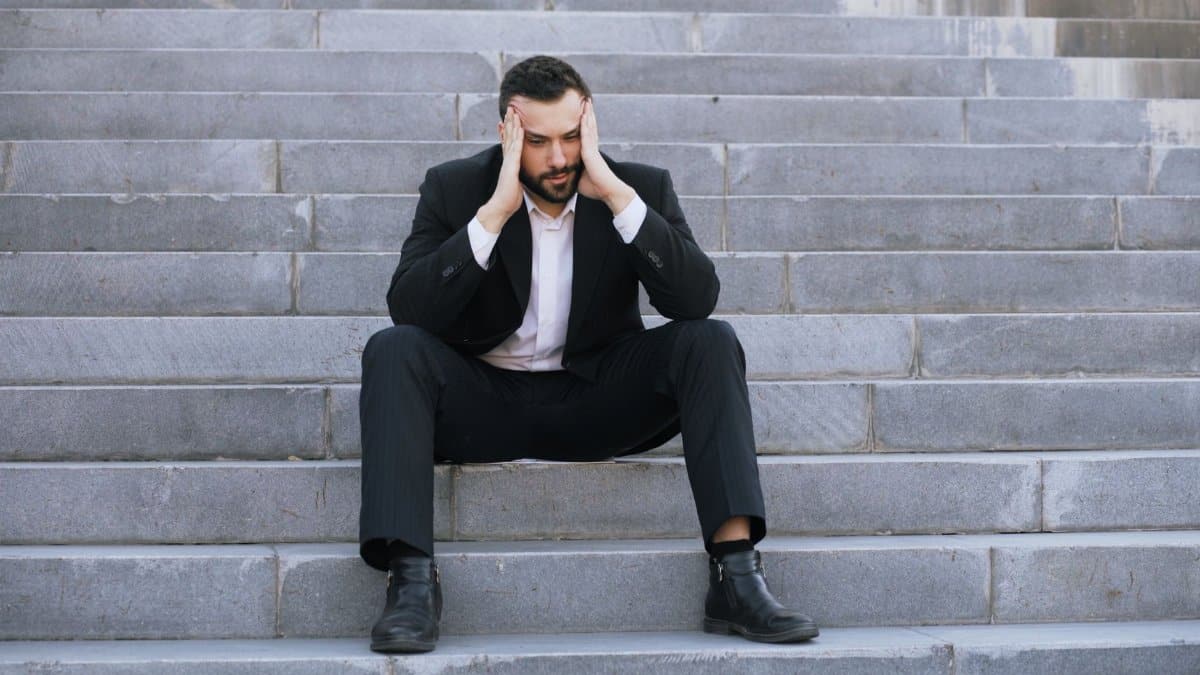 Businessman in a suit experiencing stress while seated on outdoor steps.