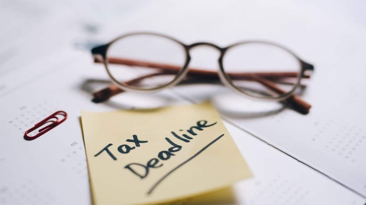 A close-up shot of a sticky note with 'Tax Deadline' written on it, alongside eyeglasses and a calendar.
