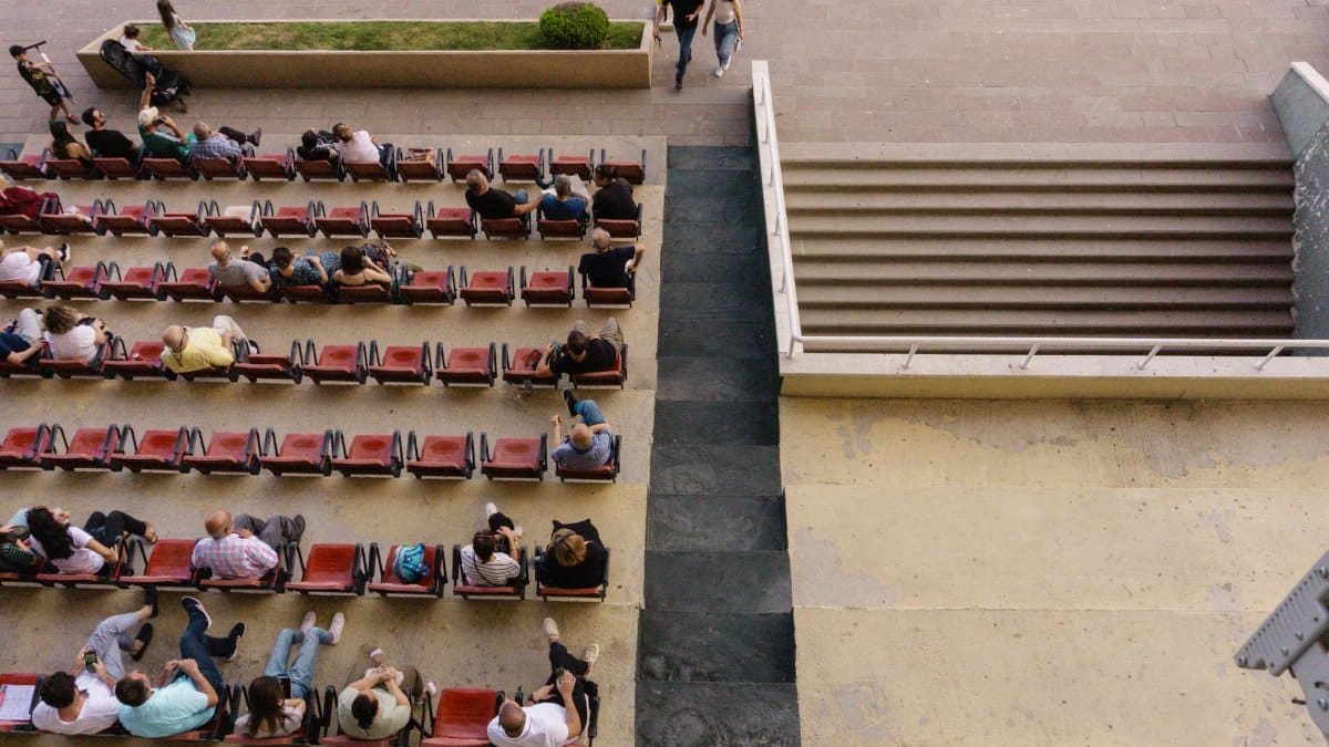 Aerial view of an outdoor auditorium with people seated in rows, next to stone steps.