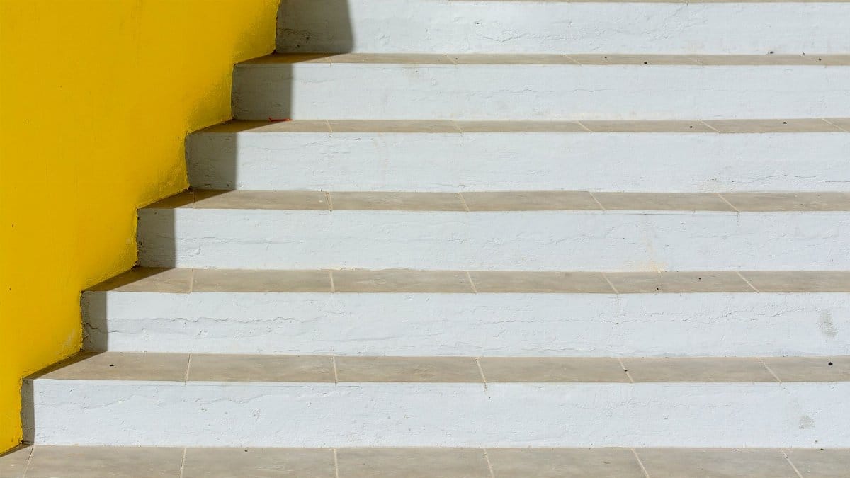 A minimalist staircase with white steps and a vibrant yellow wall. Modern design.