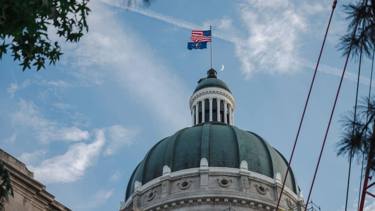 The Indiana State Capitol dome with American and Indiana flags flying against a bright blue sky.