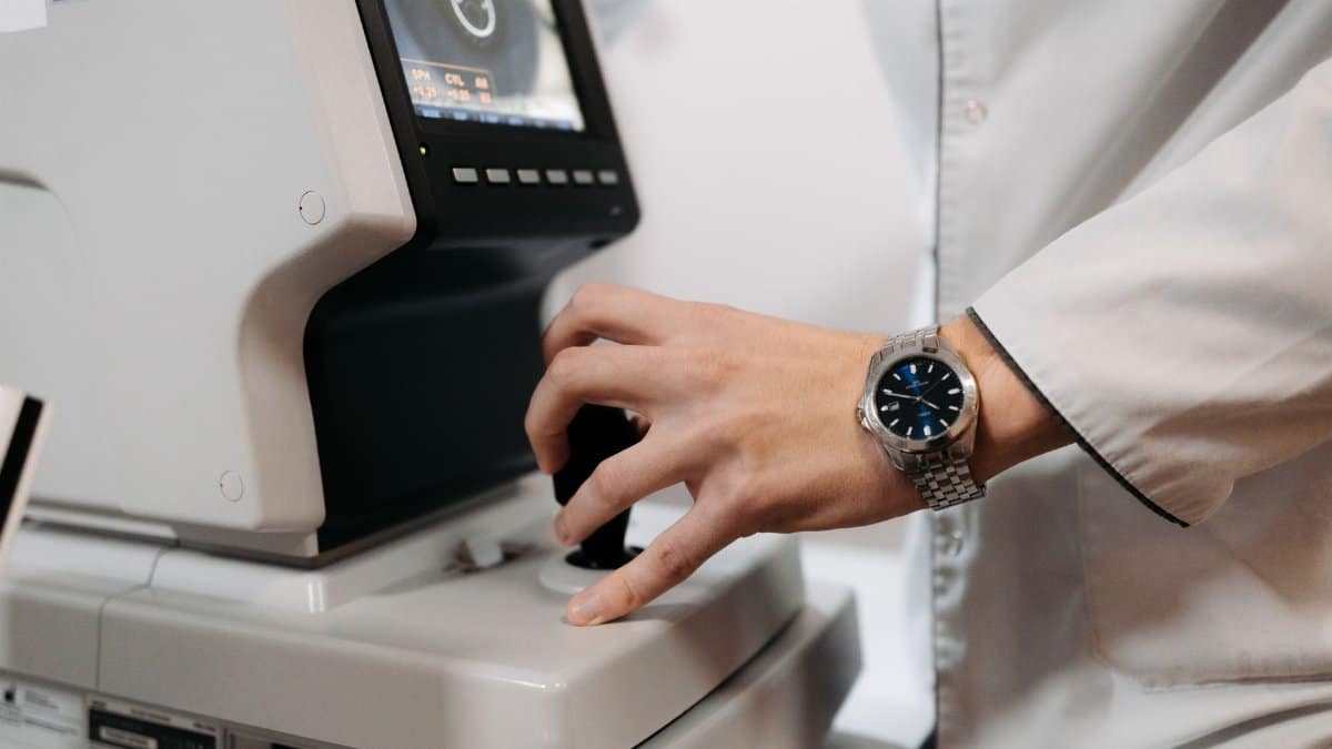 A doctor's hand operating an eye examination device in a clinical setting.