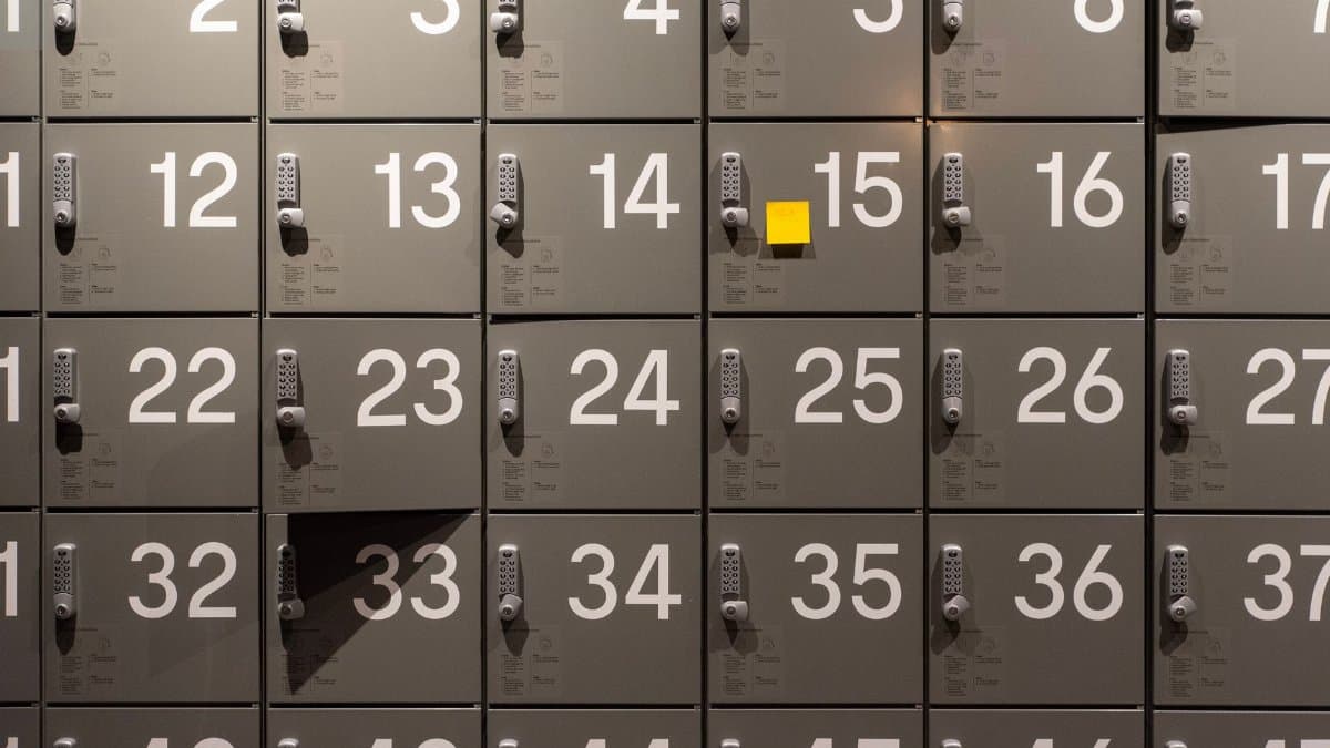 Gray lockers with electronic locks featuring numbers and a single yellow sticky note in the center.