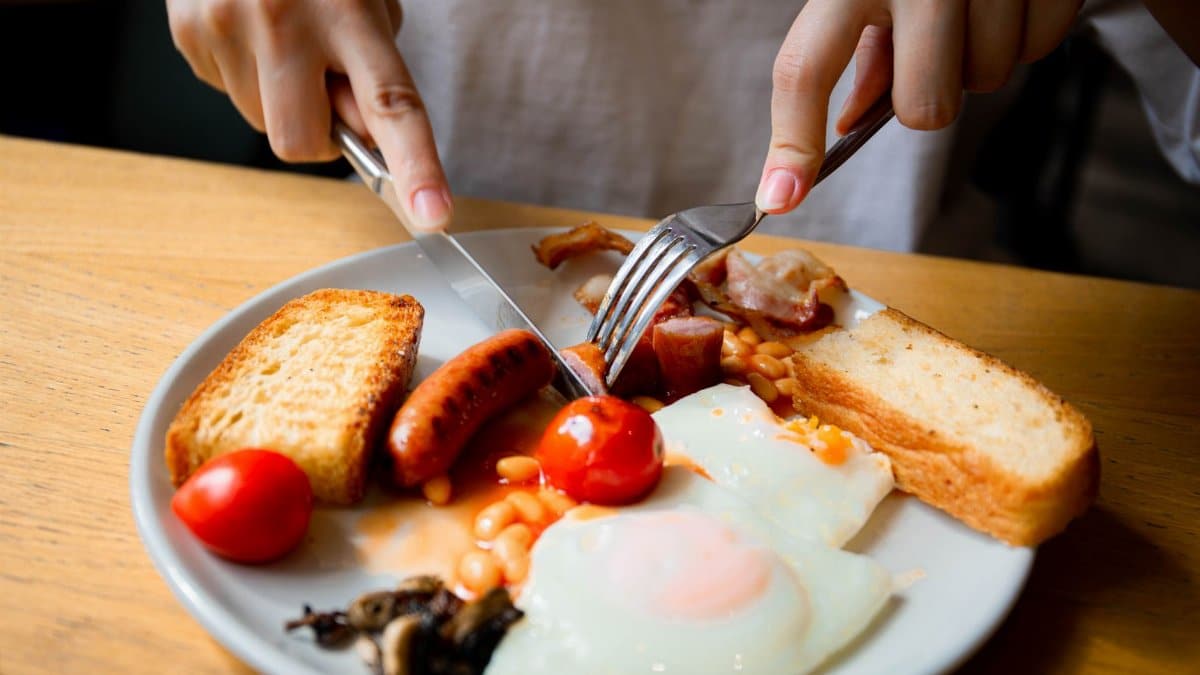 Close-up of a full English breakfast served on a plate with eggs, bacon, sausage, and tomatoes.