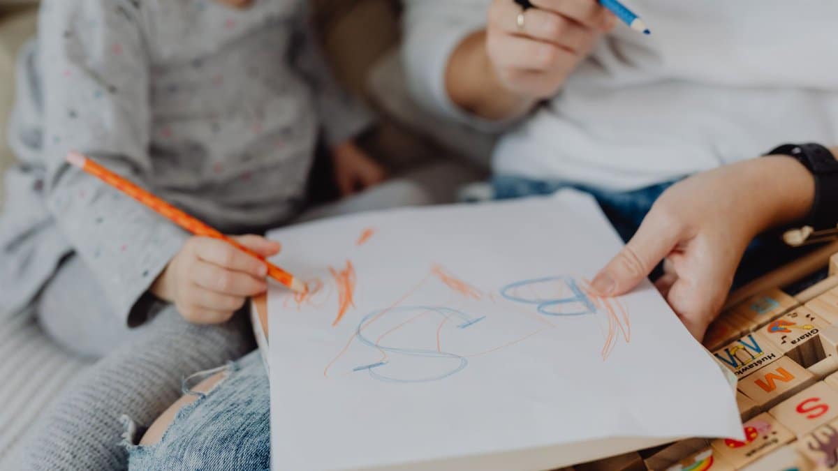 Child and parent drawing together with crayons, expressing creativity and bonding.