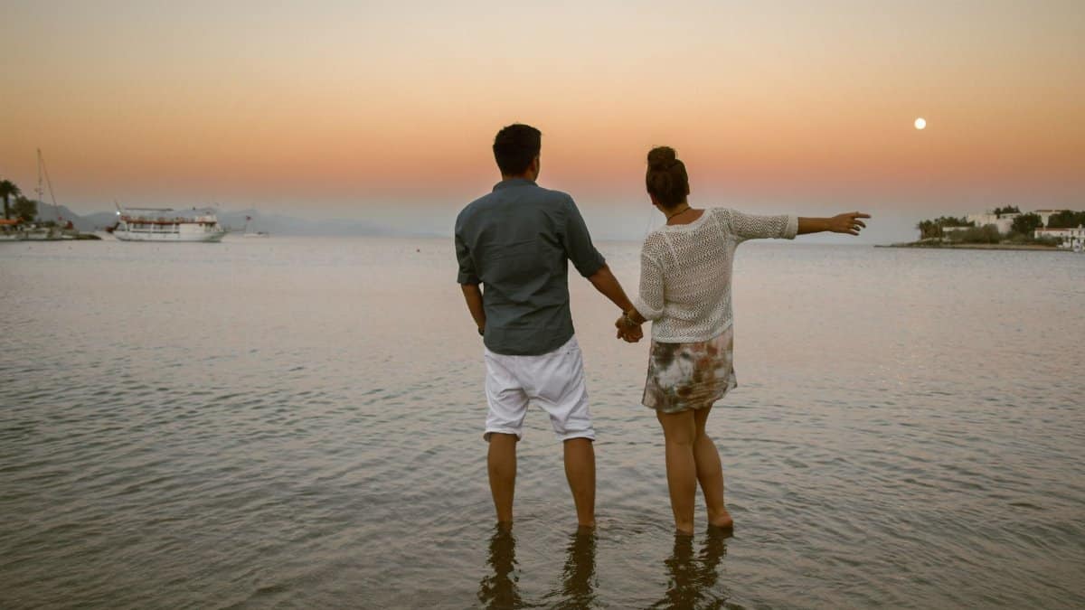 A romantic couple holding hands and enjoying a sunset view by the sea in Datça, Türkiye.