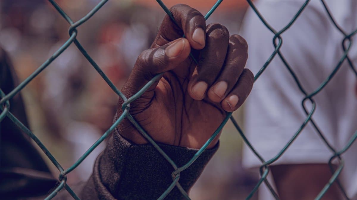 Close-up of a hand gripping a wire fence symbolizing confinement or hope.