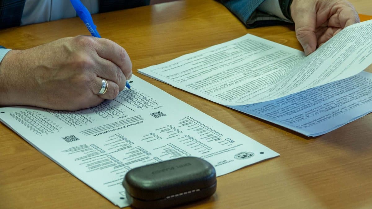 Close-up of a man filling out official documents with a pen on a wooden table.