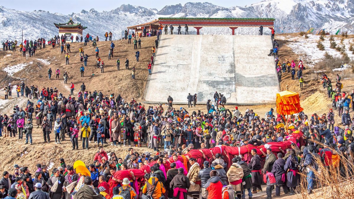 Crowds gather for a colorful Tibetan festival in a mountainous landscape with traditional architecture.