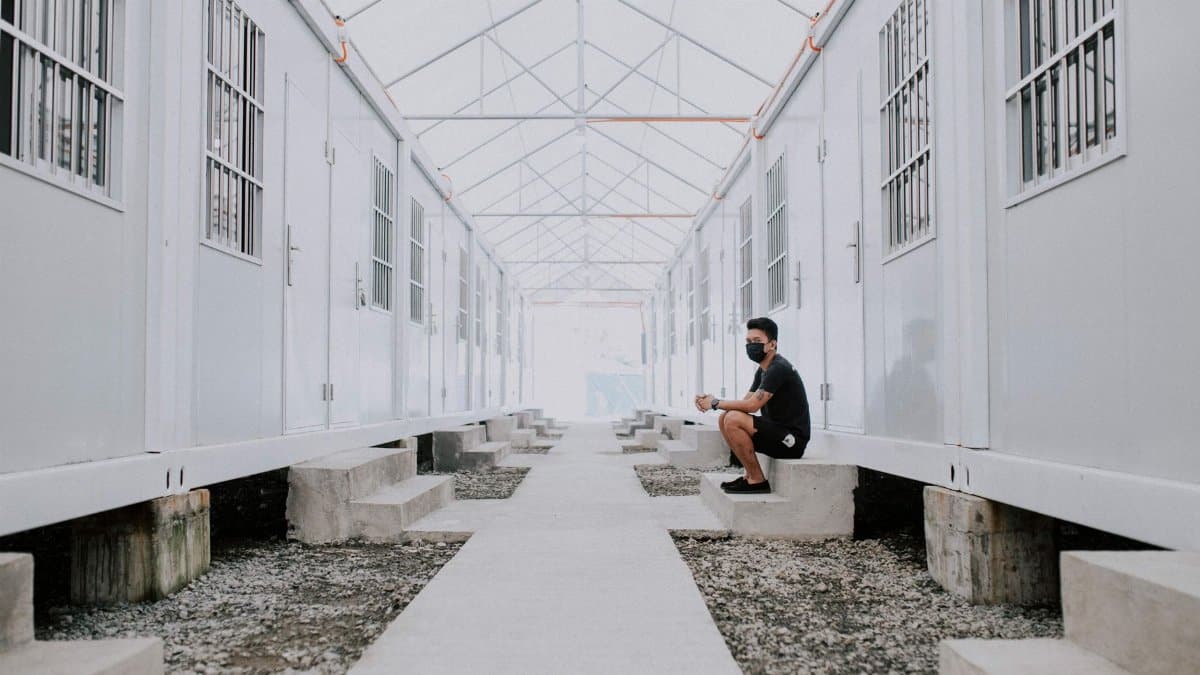 A young man wearing a mask sits outside temporary housing units in Davao City.