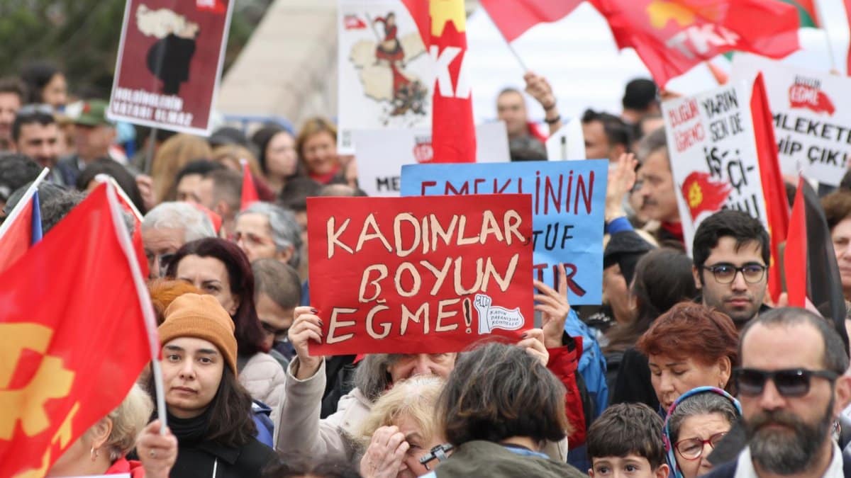 A diverse group of people in a protest holding signs and red flags, advocating for social issues.