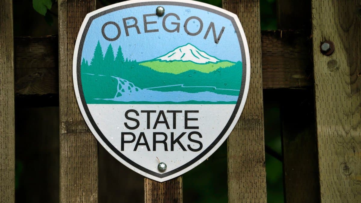 Oregon State Parks emblem sign mounted on a rustic wooden fence, surrounded by nature.