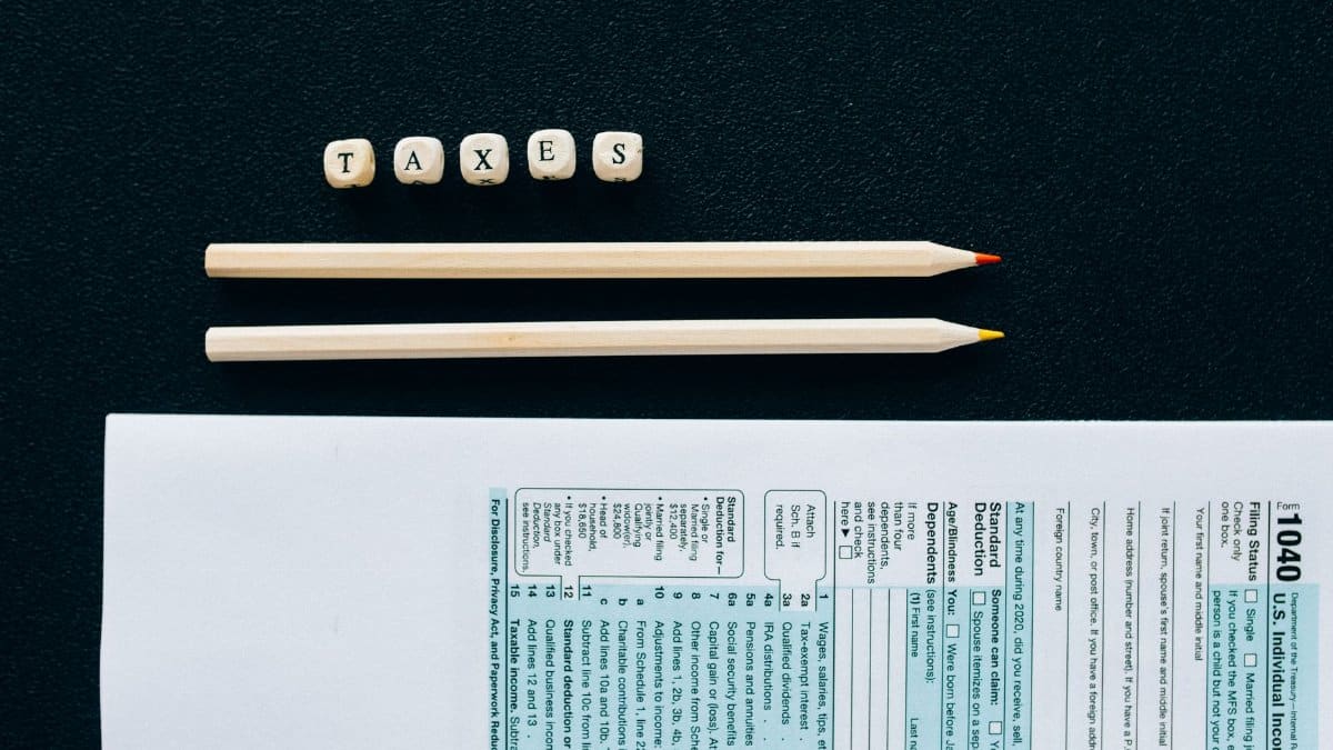 Flat lay of 1040 tax form with pencils and 'TAXES' blocks on black background.