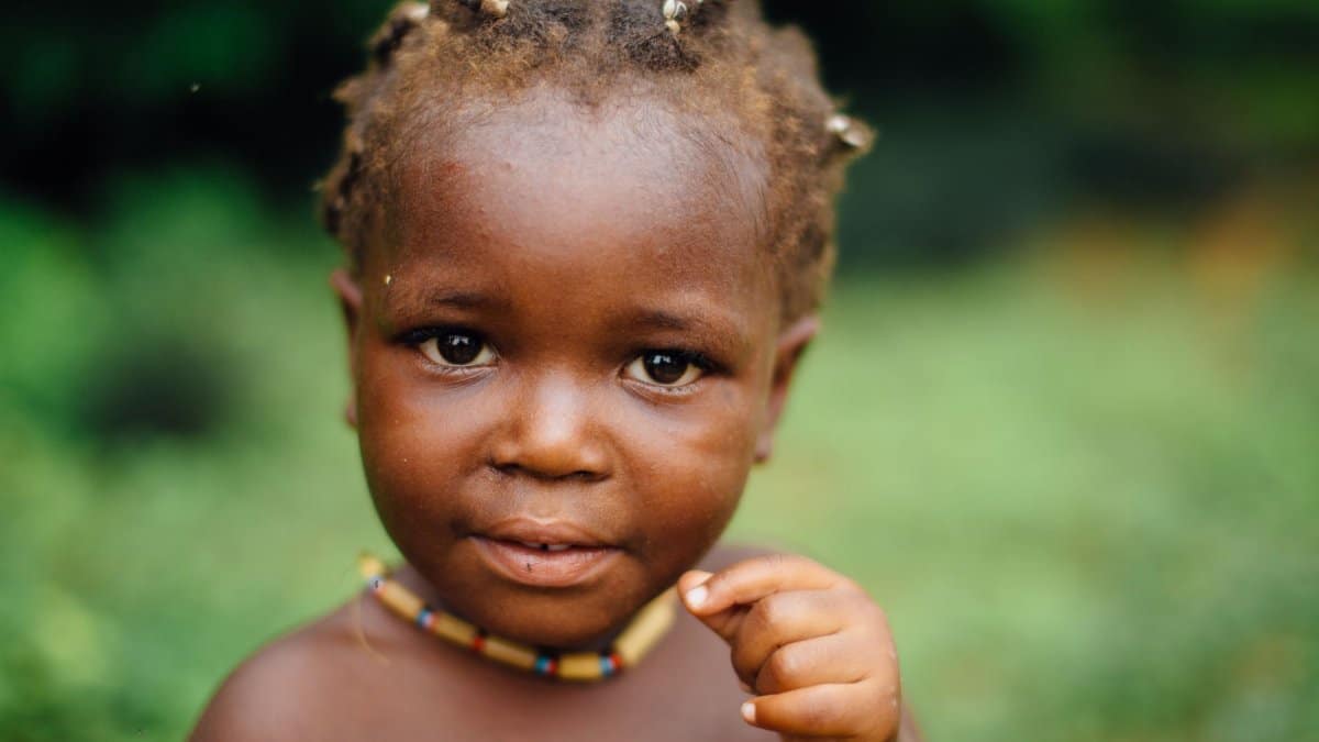 Heartwarming close-up portrait of a young Haitian child with vibrant necklace, captured outdoors.