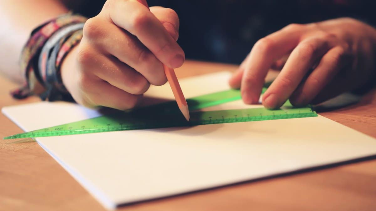 A person using a pencil and ruler to draw lines on paper, ideal for education and design concepts.