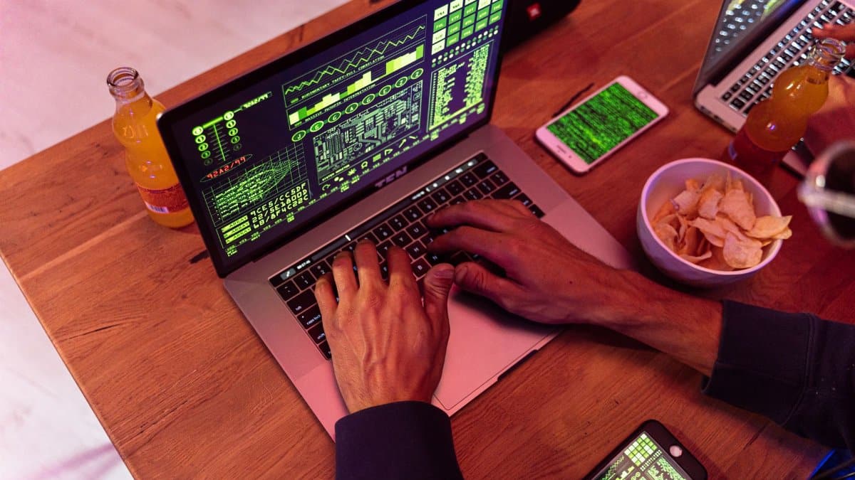 Hands typing on a laptop with coding, phone on desk, symbolizing cybersecurity.