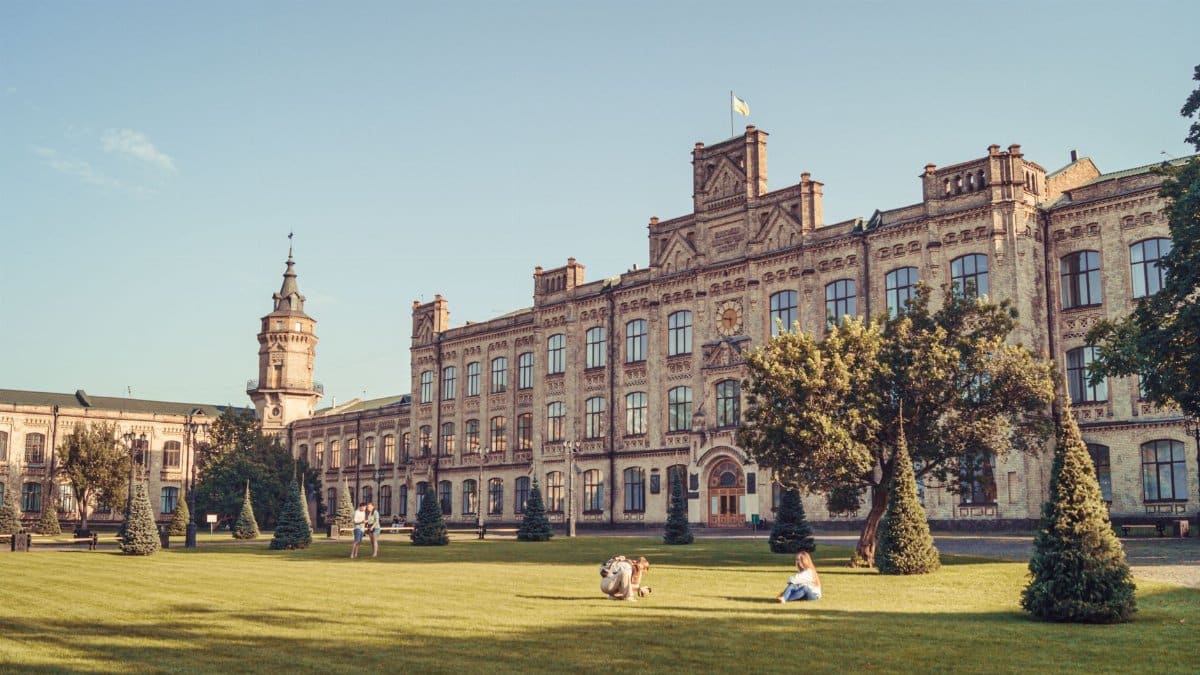 A beautiful historic university building in Kyiv, Ukraine, surrounded by a lush green lawn and trees on a sunny day.