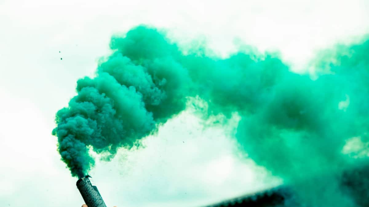 Low angle of crop anonymous person demonstrating bright smoke bomb against clear sky