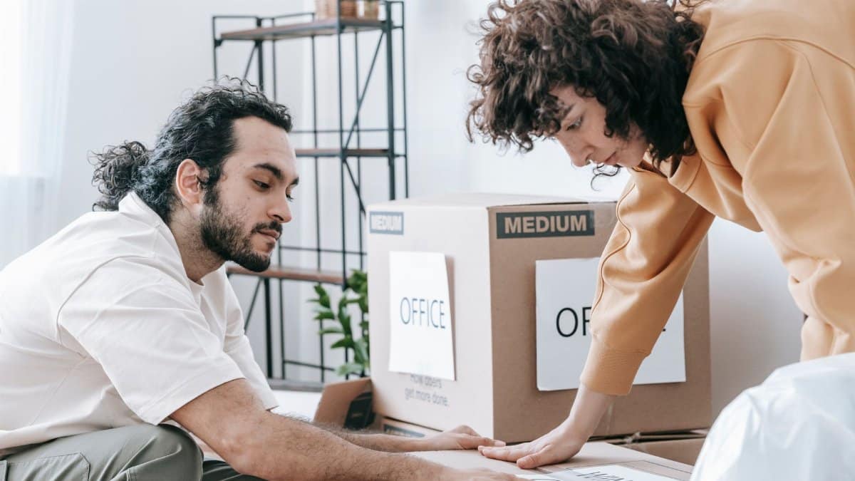 A couple packing and organizing office supplies into labeled boxes, preparing for relocation.