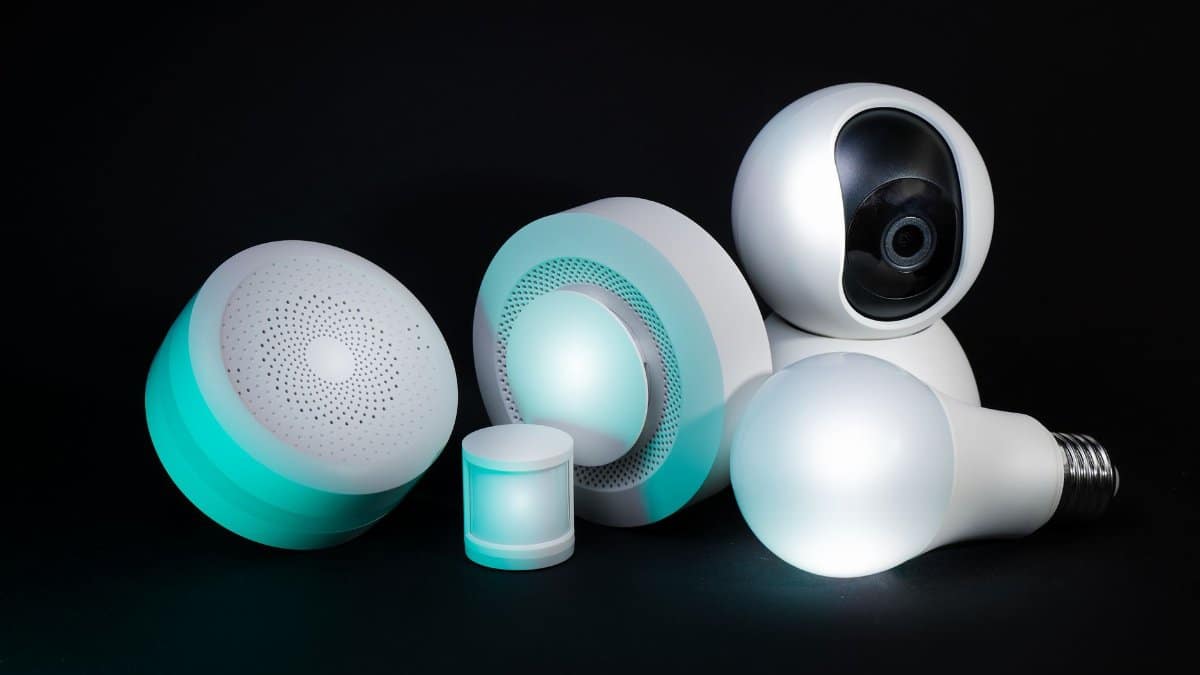Collection of smart home devices including a camera, bulbs, and sensors on a dark background.