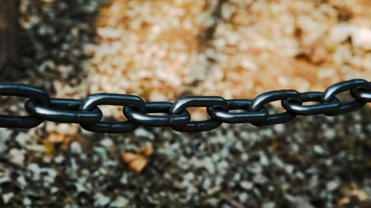 Detailed view of a sturdy black metal chain outdoors on a blurred background.
