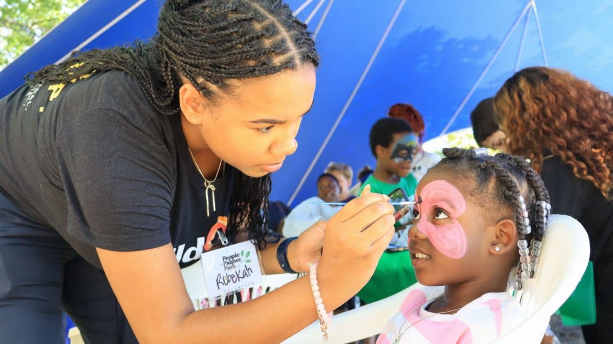 A young woman paints a child's face at an outdoor festival, enhancing community joy and creativity.