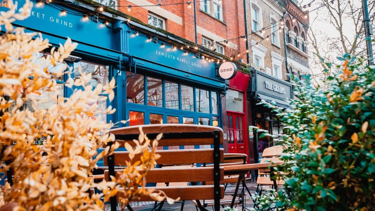 Outdoor seating at a London cafe adorned with fall foliage and string lights.