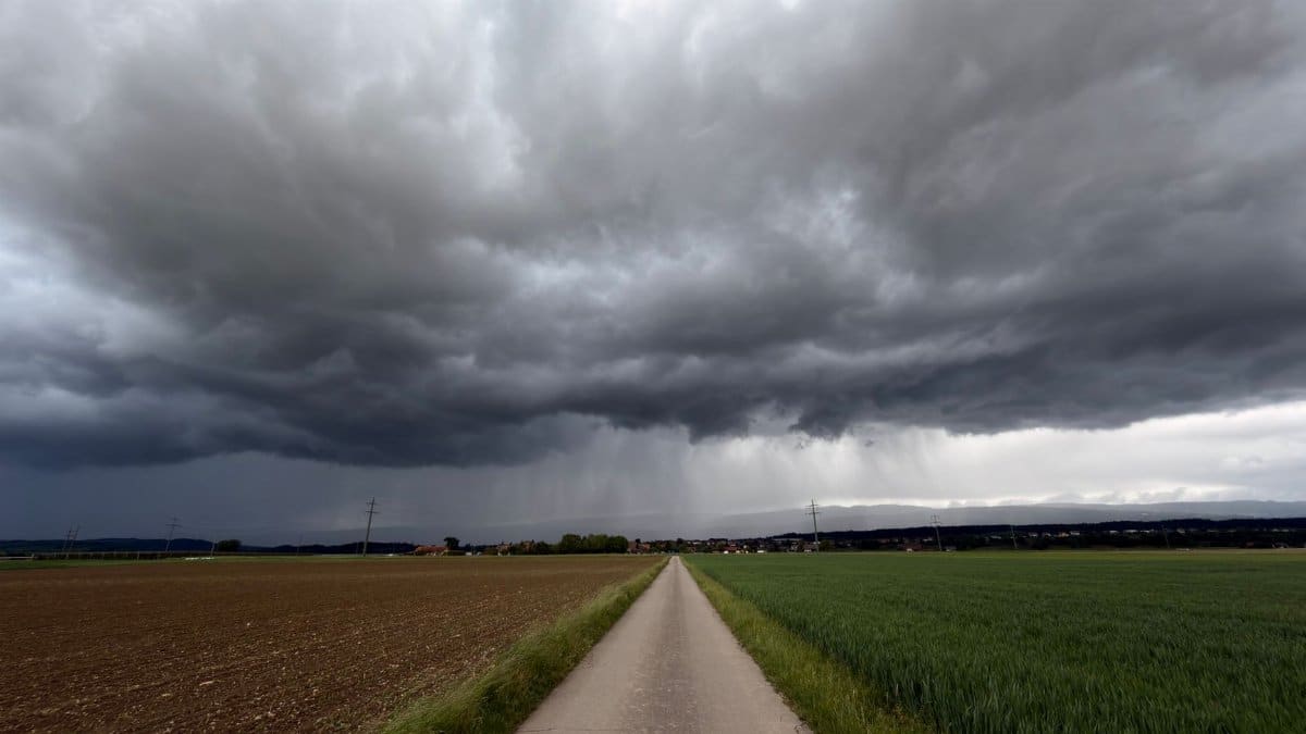 Looming storm clouds over a rural path and fields in Swiss countryside.
