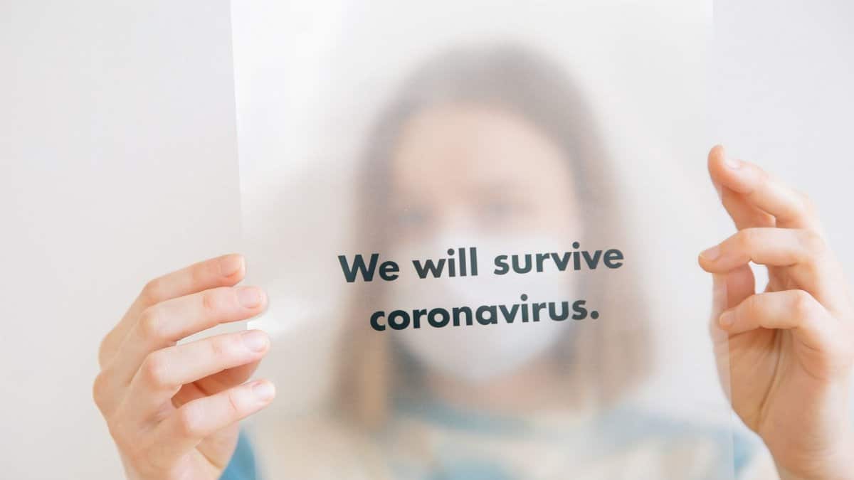 A person holds a sign saying 'We will survive coronavirus,' conveying hope during the pandemic.