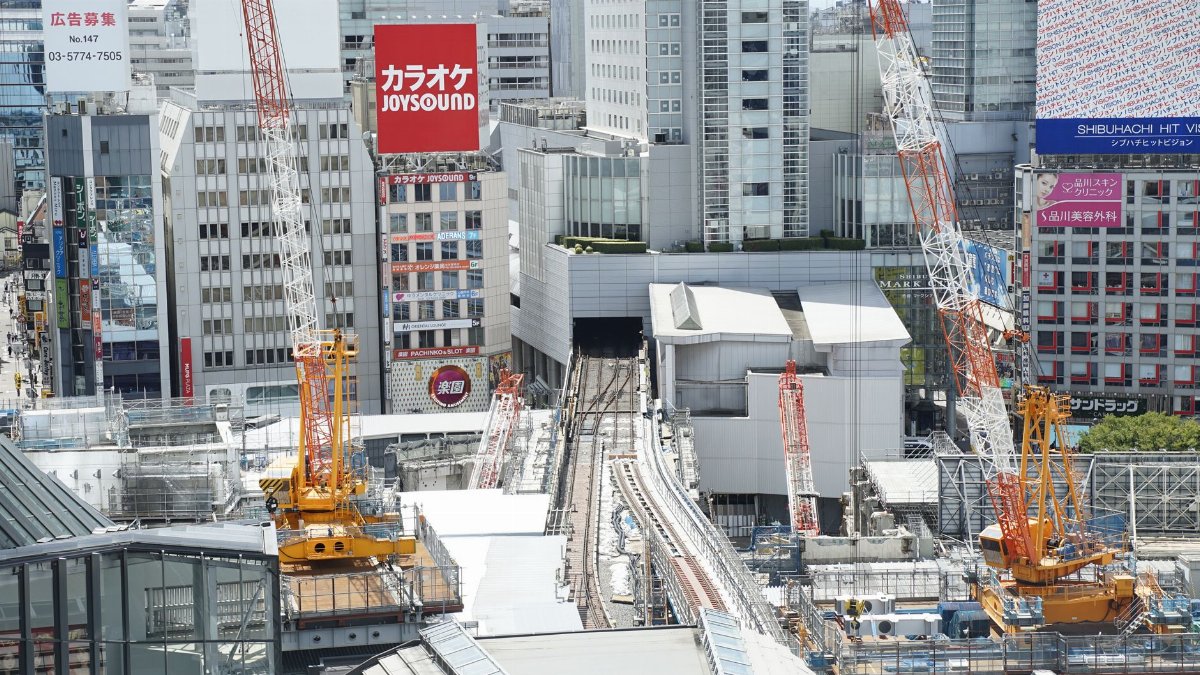 Aerial view of construction cranes in Shibuya, Tokyo with skyscrapers.