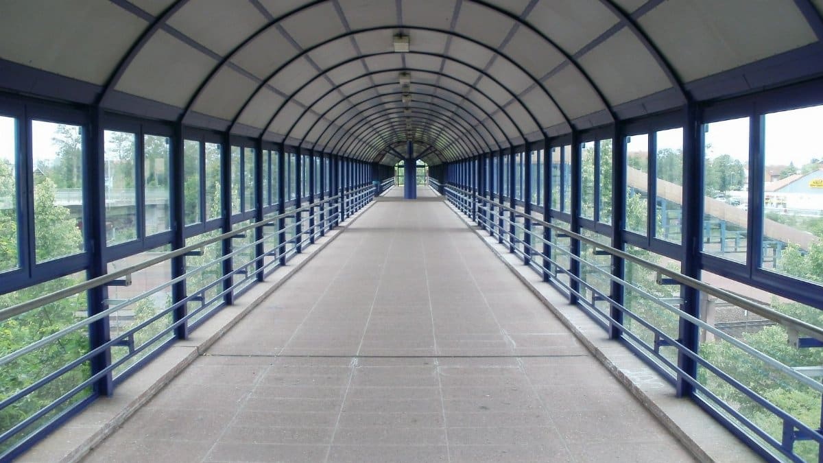 A wide covered pedestrian bridge with geometric design elements in a modern urban setting.