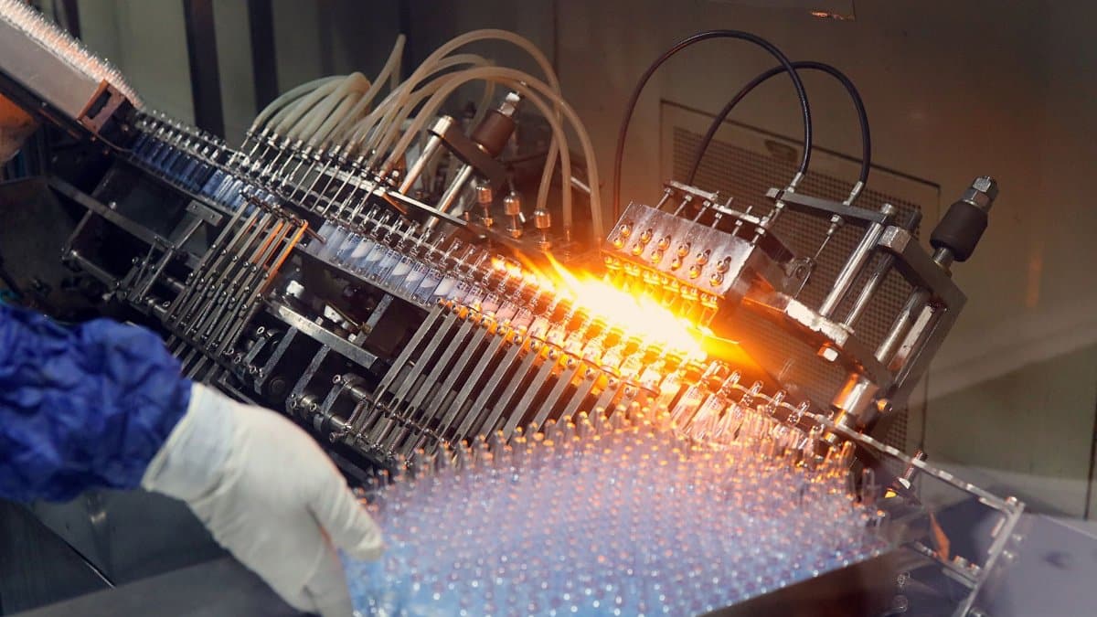 Close-up of ampoule filling and sealing in a pharmaceutical manufacturing line.