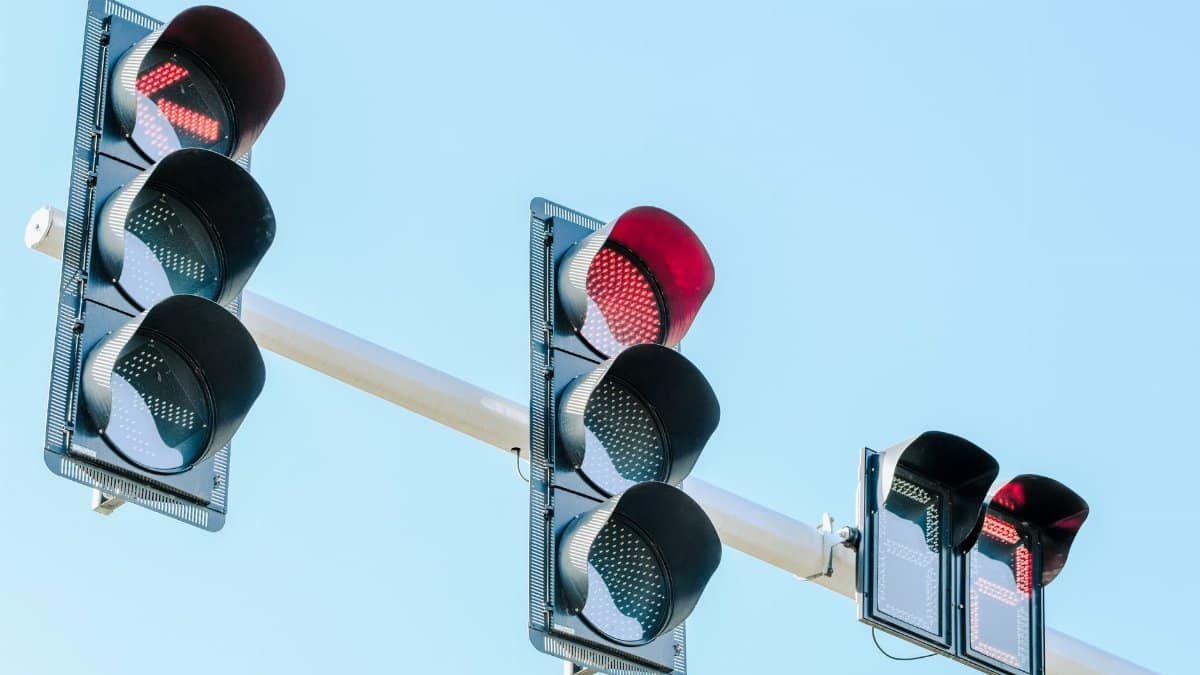 Traffic lights showing red against a clear blue sky on a sunny day.