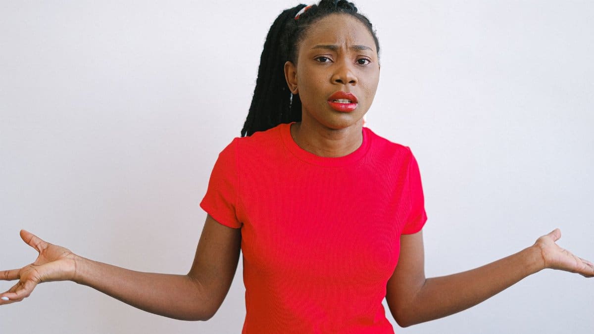 Young black woman in a red shirt with a confused expression. Perfect for emotive stock photo needs.