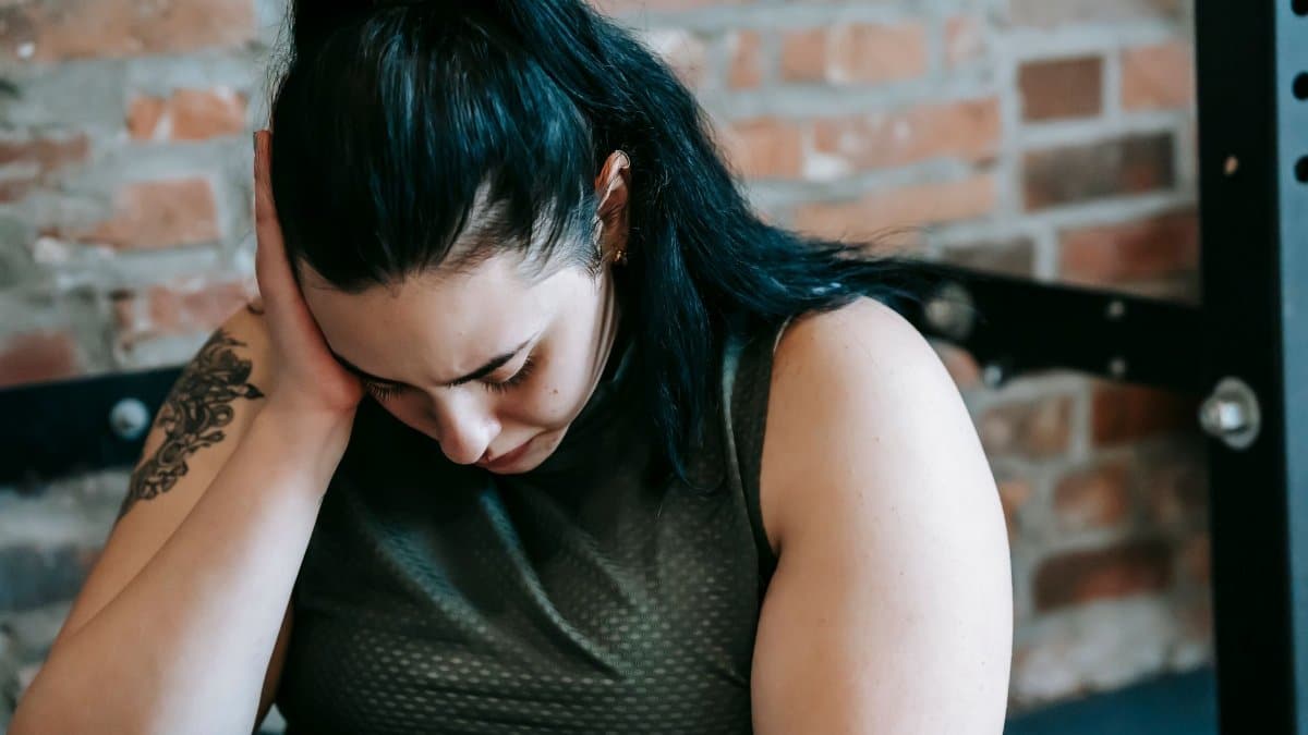 Upset female sitting near sports equipment and feeling desperate and hopeless at training in fitness club
