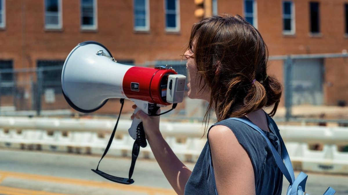 A young woman passionately speaking into a megaphone during a peaceful protest on a sunny day.