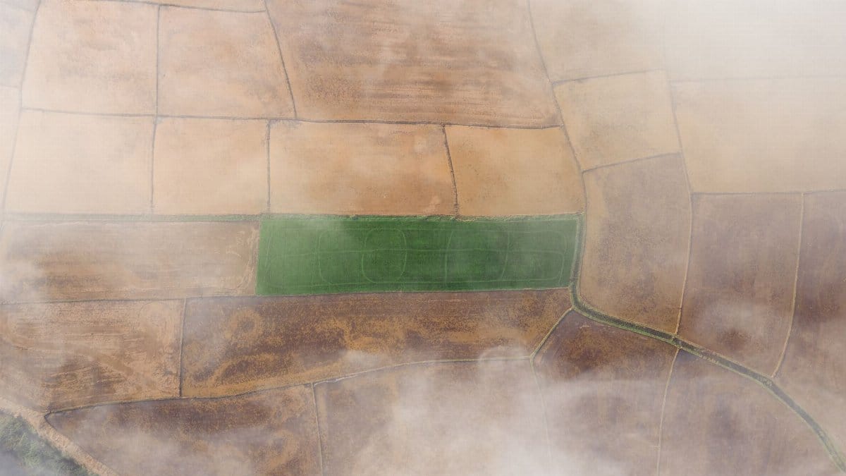 A stunning aerial shot of patchwork farmland with a vibrant green field amidst fog.