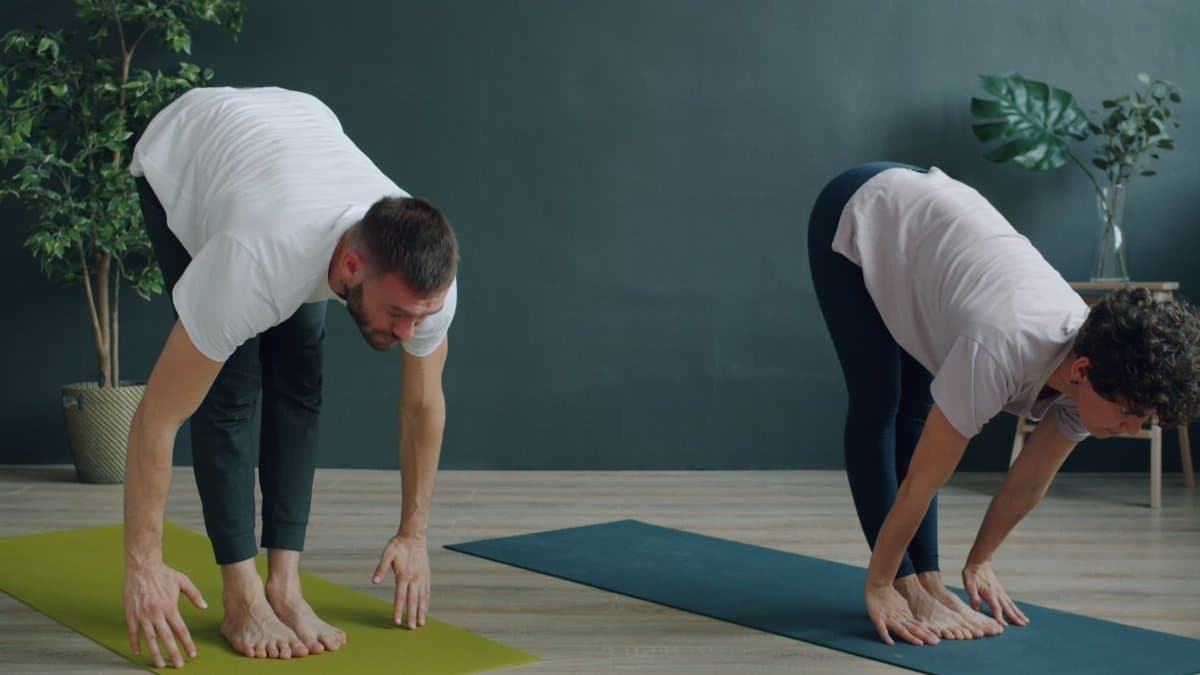 Two individuals performing yoga stretches on mats in a serene indoor setting.