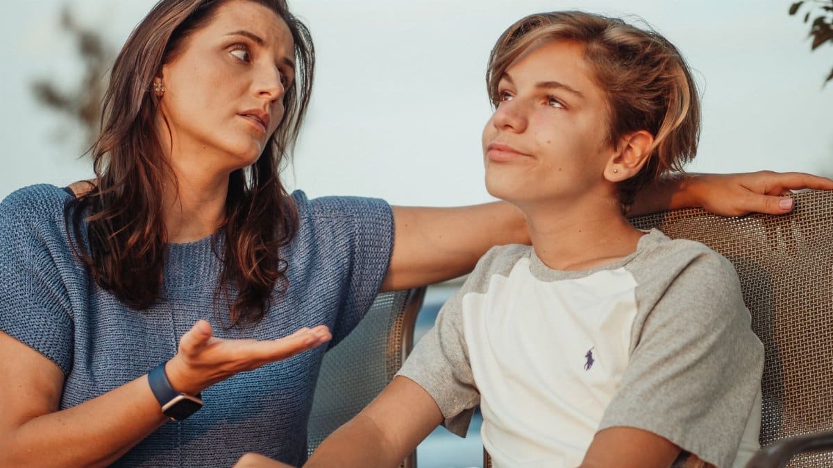 A mother and her teenage son engage in a conversation sitting outside, expressing familial warmth and connection.
