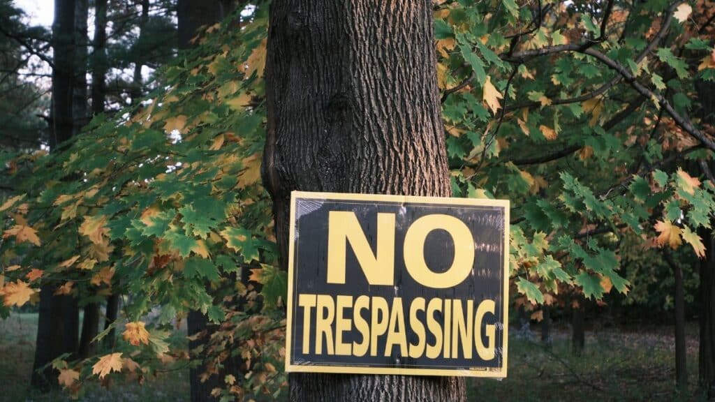 A no trespassing sign displayed on a tree surrounded by autumn foliage.