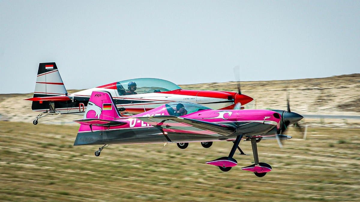 Two colorful aerobatic planes perform synchronized flying over a landscape.