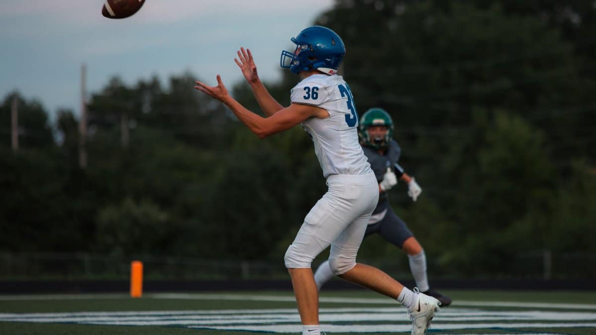 High school football players in action on the field catching a pass during a game.