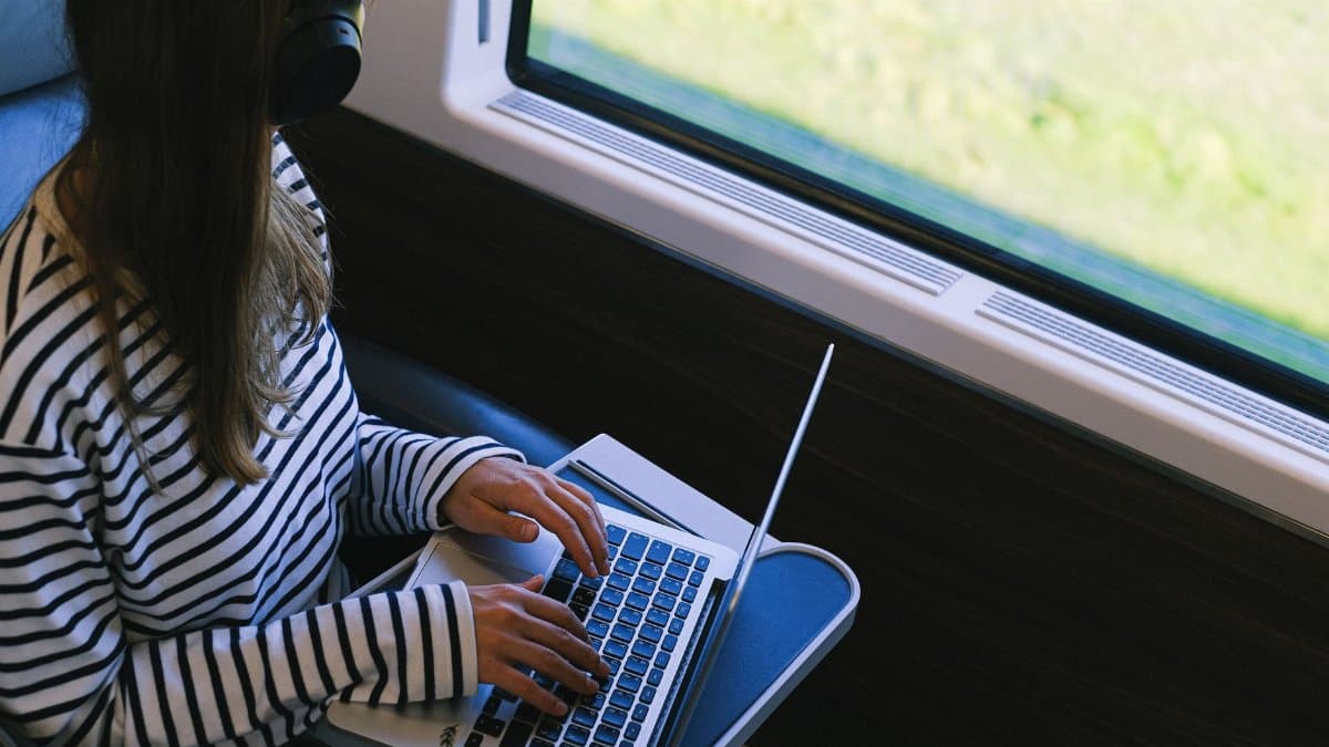 Person with headphones using laptop on a train, symbolizing remote work and digital nomad lifestyle.