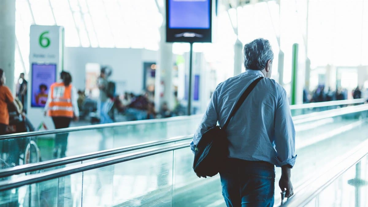 An adult male walking on an airport travelator, captured in a modern and well-lit terminal.