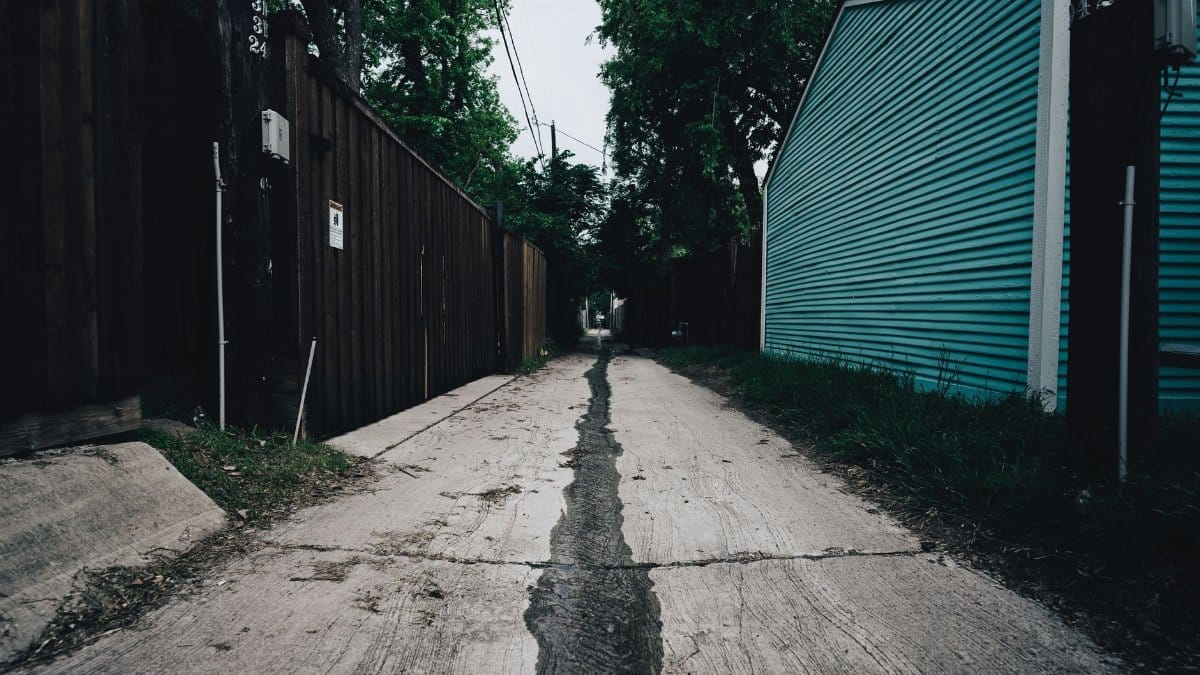 Empty narrow alleyway with a wooden fence and grass, offering a moody atmosphere.