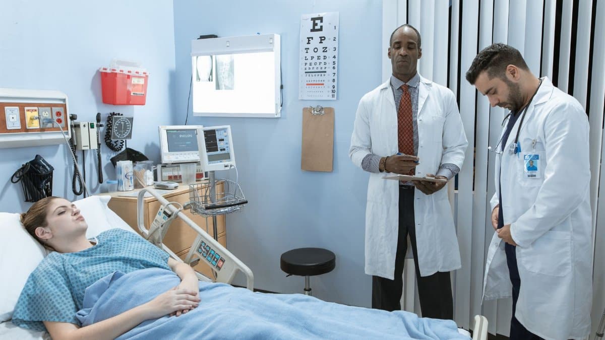 Doctors in lab coats attend to a patient lying in a hospital bed, emphasizing healthcare and medical care.