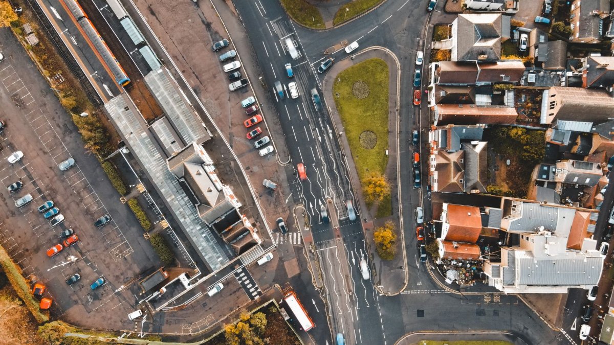 Aerial view of various vehicles driving on asphalt road near typical residential houses in suburban district on sunny day