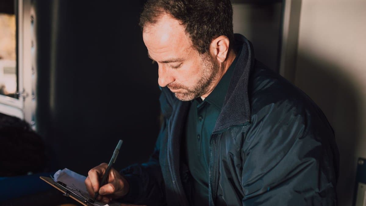 Adult male writing notes on a clipboard inside. Concentrated and thoughtful atmosphere.