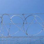 Detailed image of barbed wire fence under clear blue sky, symbolizing security and restriction.