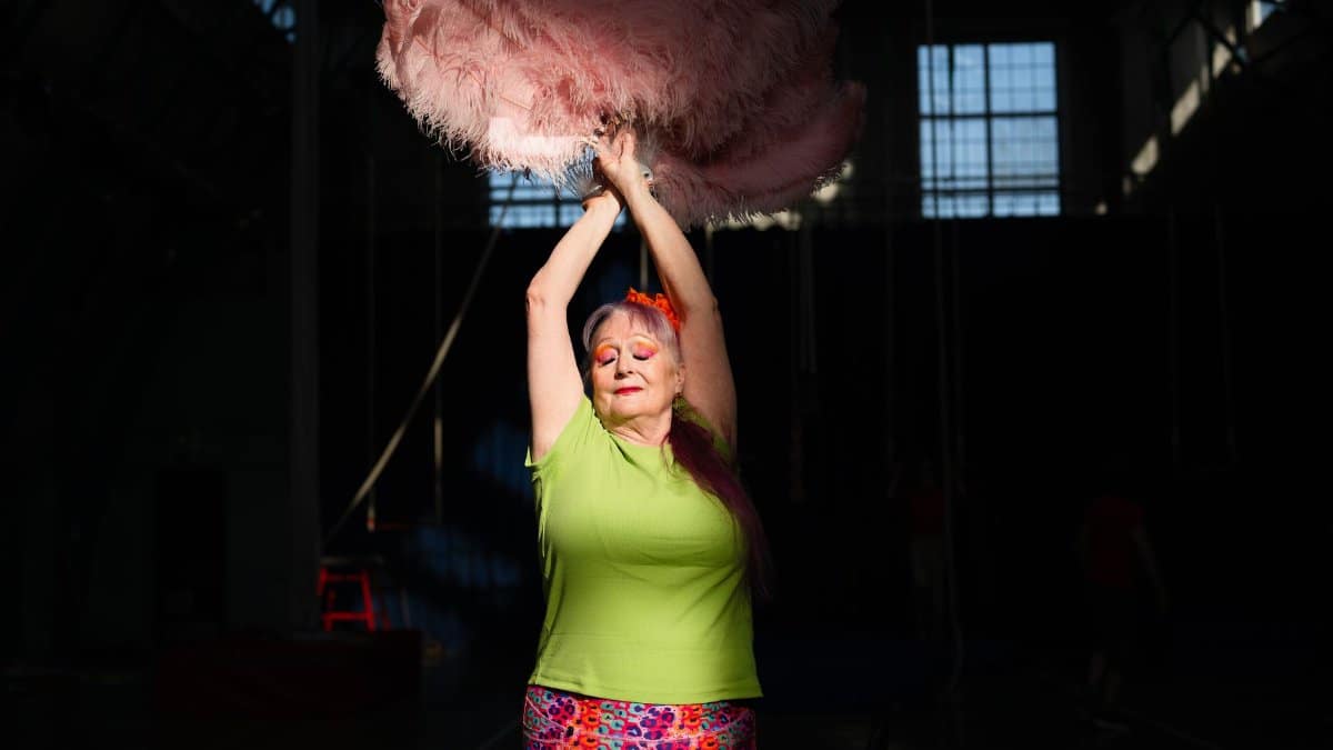 A lively performance in colorful attire and feather props at an indoor venue.